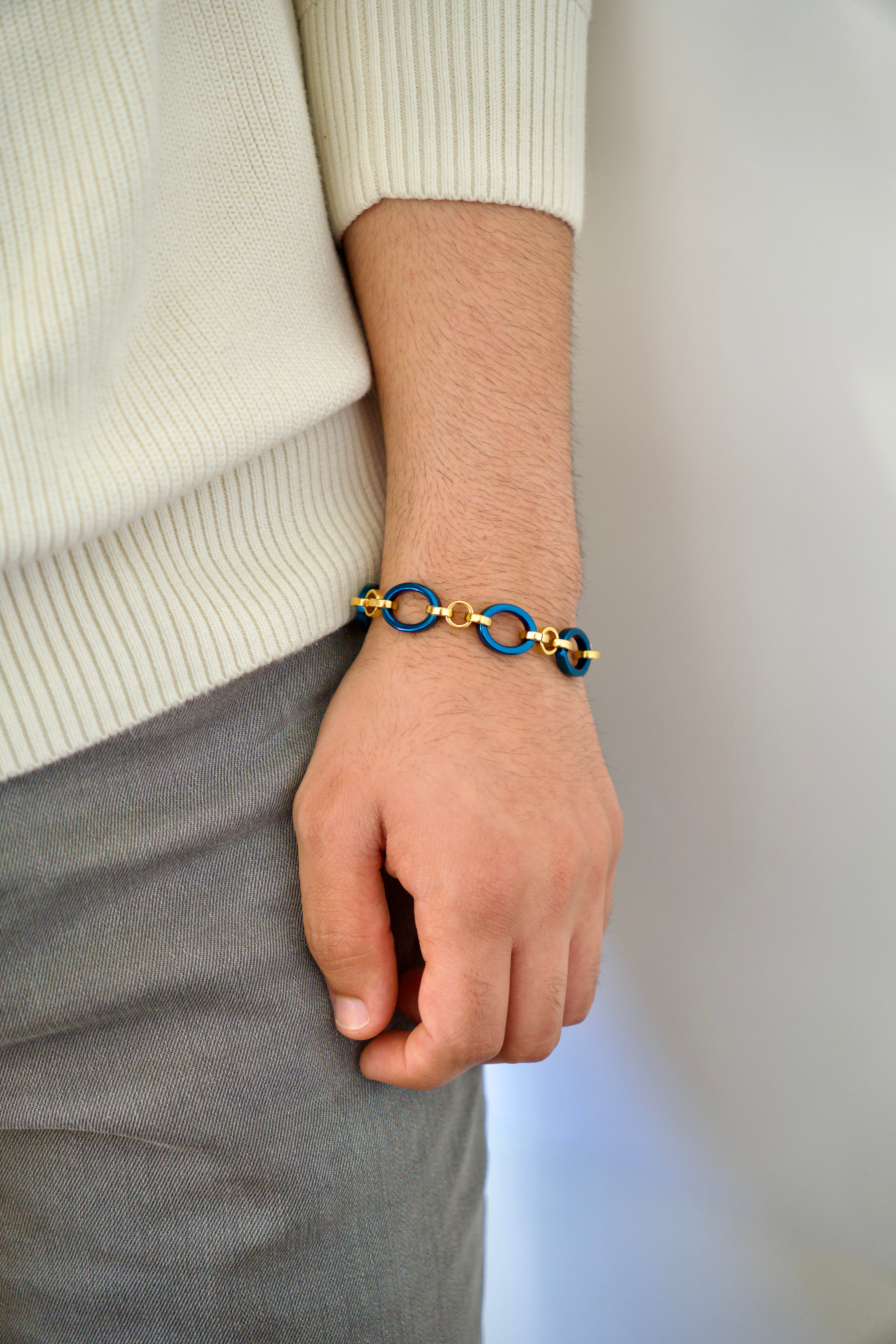 Man wearing a gold and blue bracelet on a neutral background