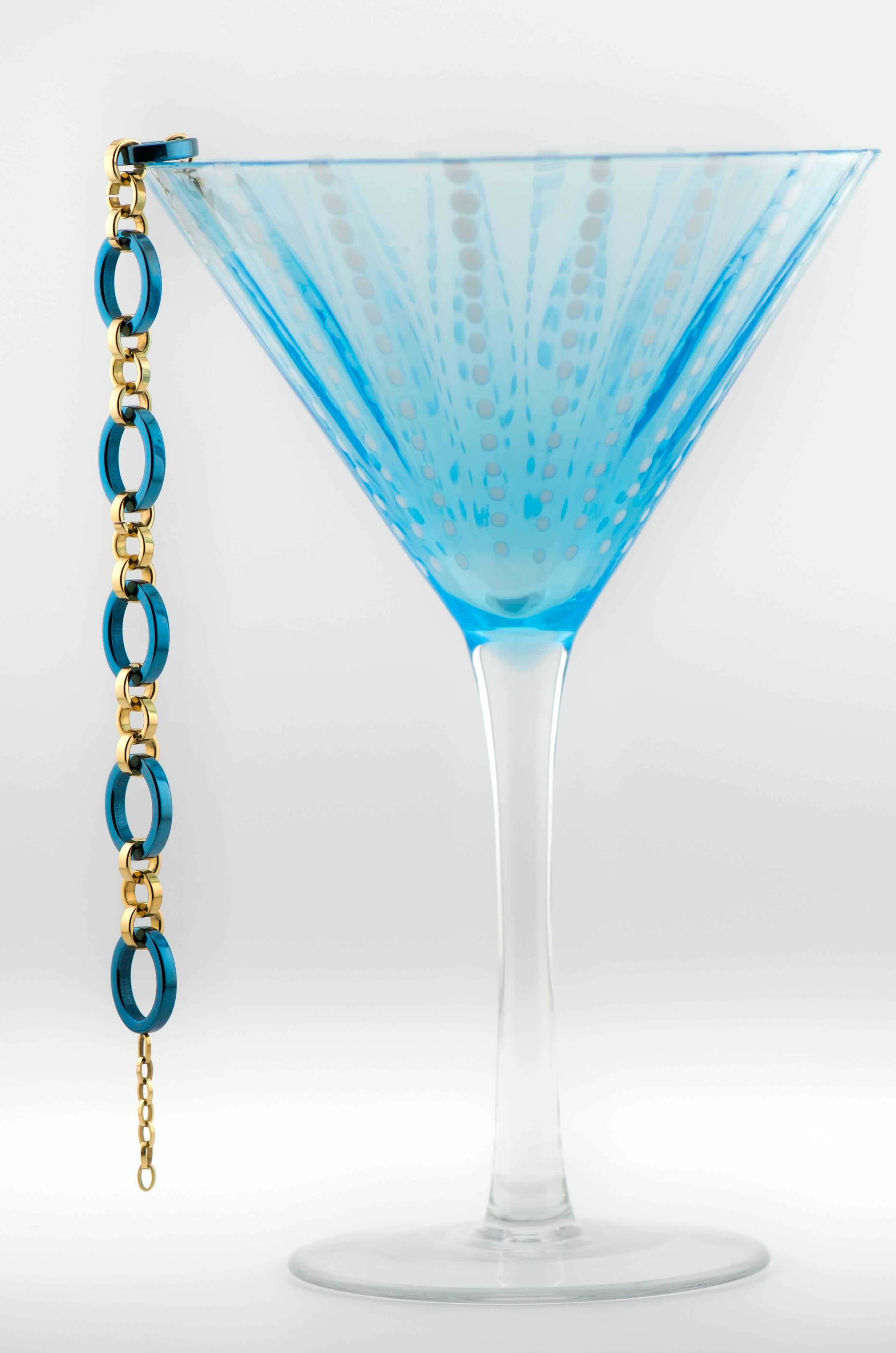 Blue martini glass with a blue and gold chain bracelet on a white background