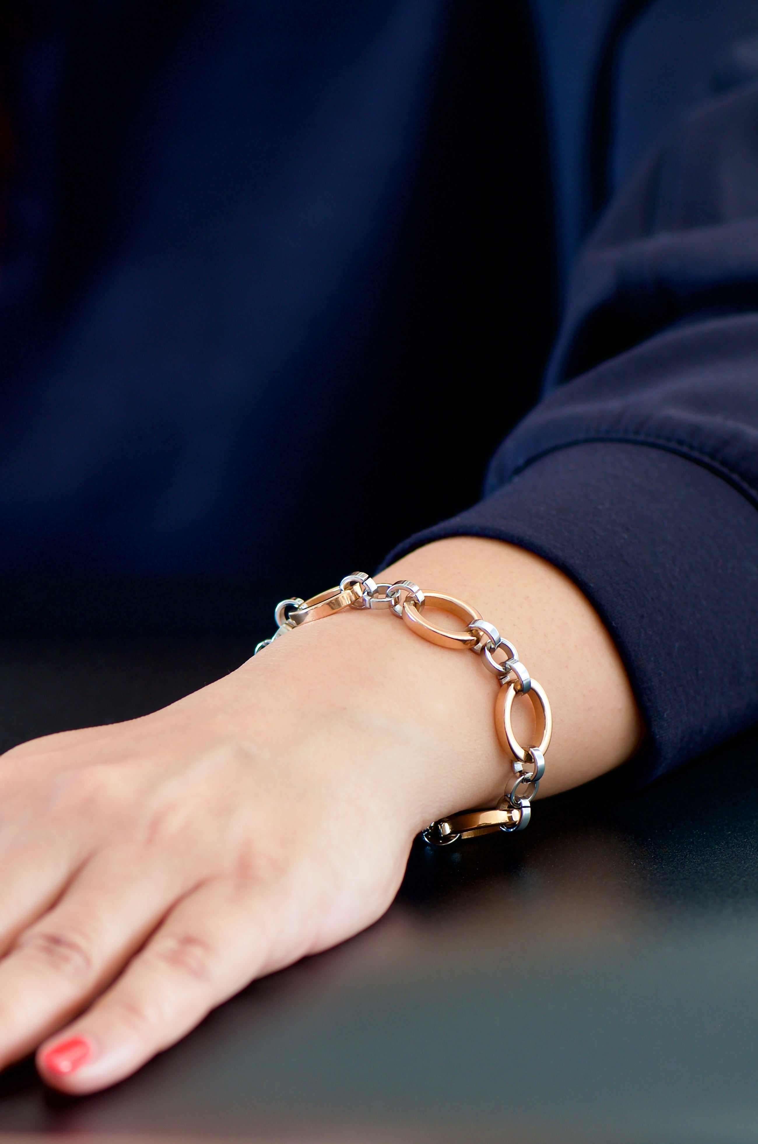 Close-up of a hand wearing a rose gold and white gold bracelet on a dark surface