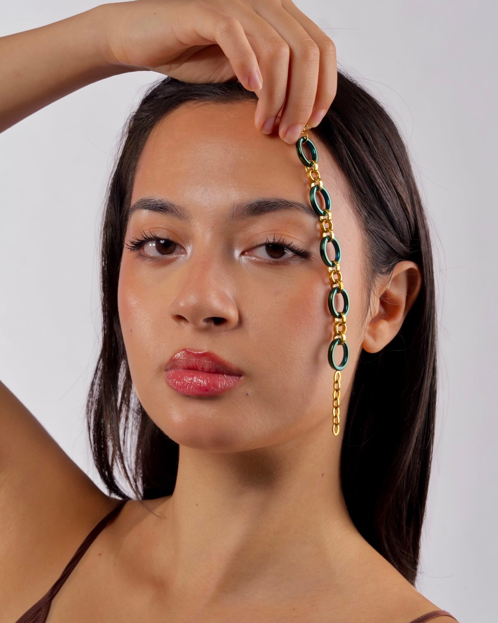 Women's wrist wearing Reversible Meridian Chain Bracelet in Green Lagoon, deep green titanium & 18K yellow gold PVD, studio - bracelet held against face
