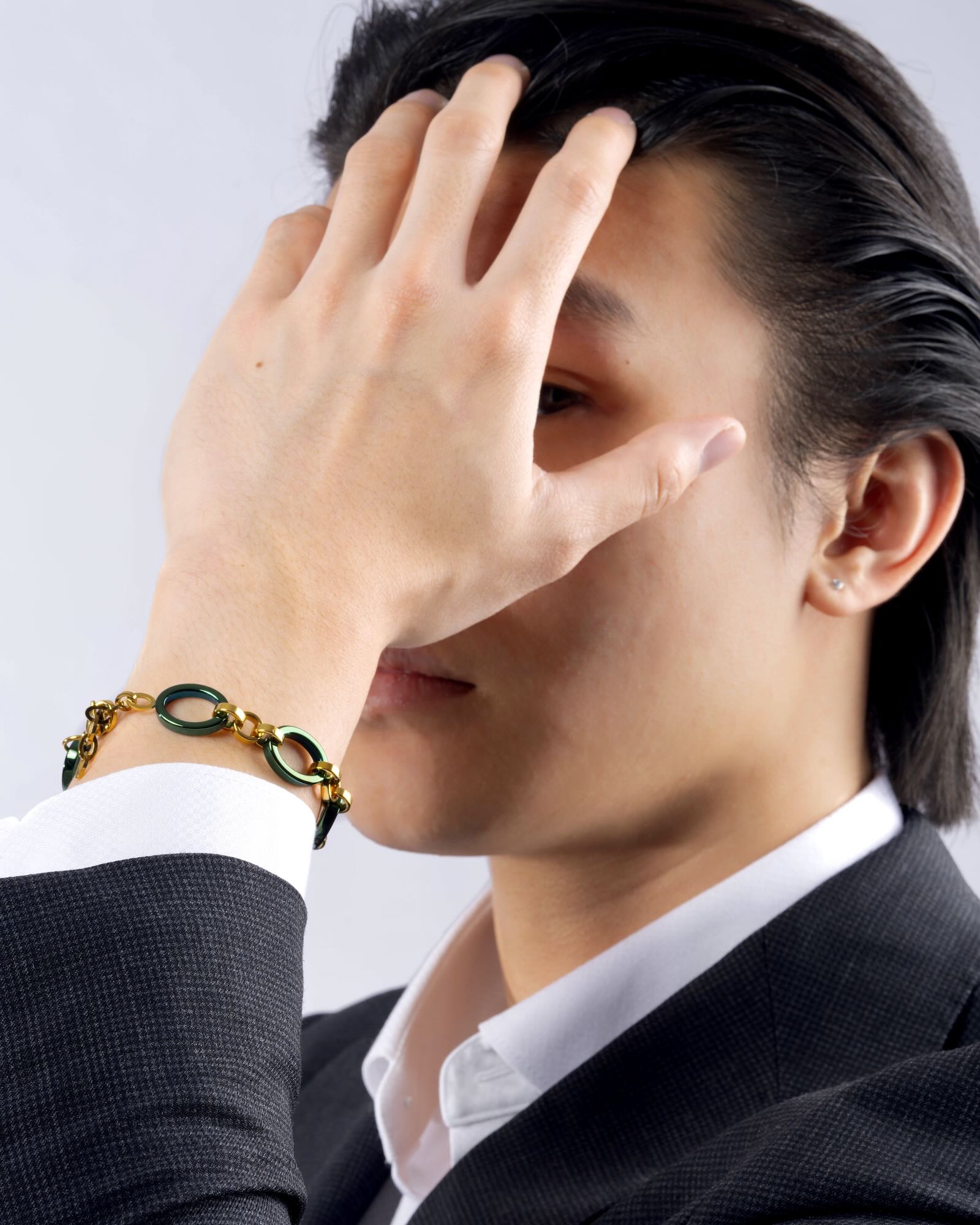 Men's wrist wearing Reversible Meridian Chain Bracelet in Green Lagoon, deep green titanium & 18K yellow gold PVD, studio - hand raised covering face