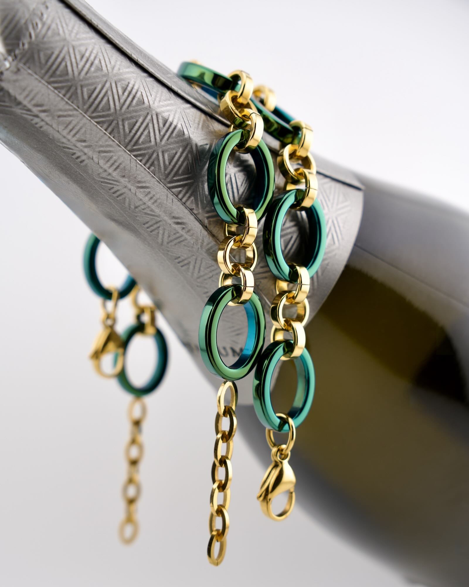 Two Reversible Meridian Chain Bracelets Green Lagoon hanging from wine bottle, showing both the deep green and vivid teal sides